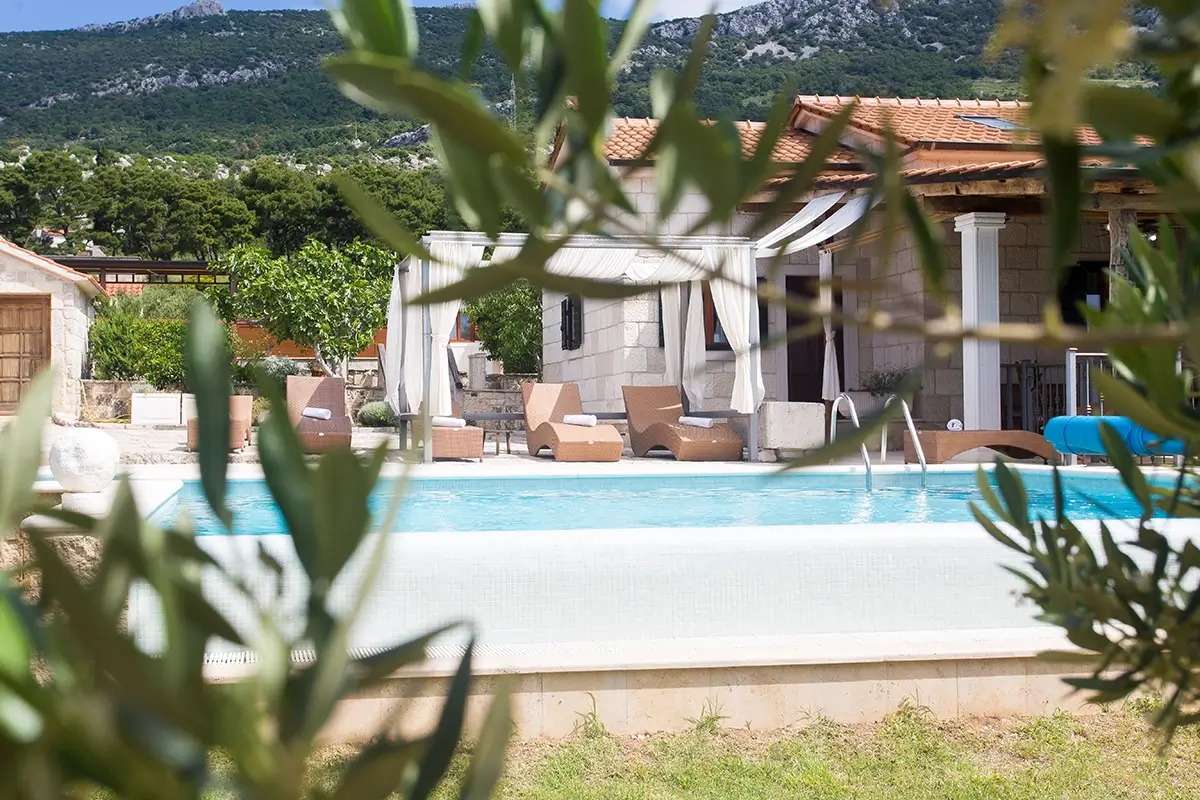 View of the villa's private pool through the branches, with lounge chairs and umbrellas by the poolside.